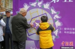 南京大屠杀幸存者葛道荣老人与小学生代表一起粘贴象征和平的紫金草。　蔡美婷 摄 - 江苏新闻网